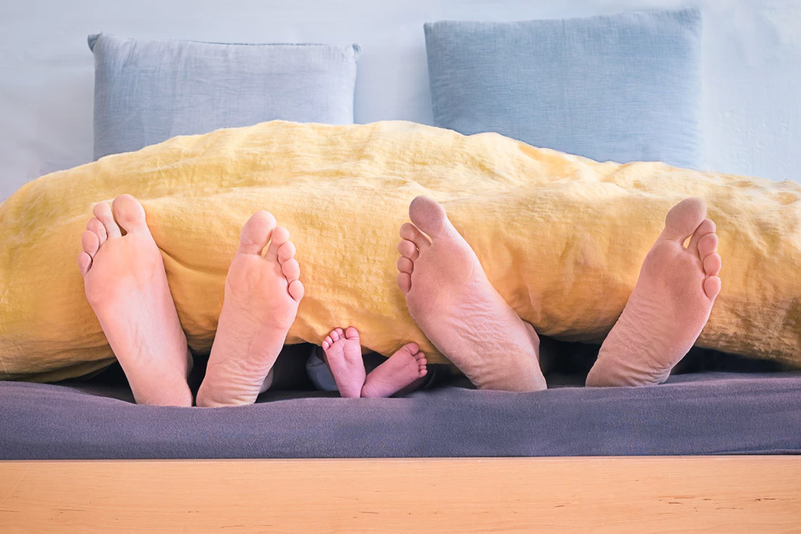 Trois paires de pieds – deux paires d'adultes et une paire d'enfant – dépassent d'une couverture jaune sur un lit - satisfaire invite exigeant