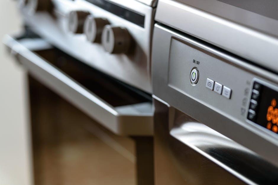 Close-up of a stainless steel oven with control knobs and a dishwasher with buttons and a digital display, both built into a modern kitchen - airbnb cleaning tips