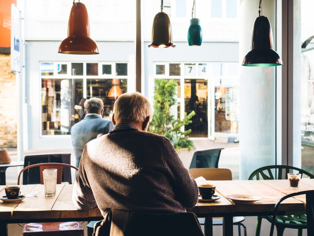 Un homme âgé est assis seul à une table dans un café confortable, en train de lire ou d'écrire - hote airbnb senior
