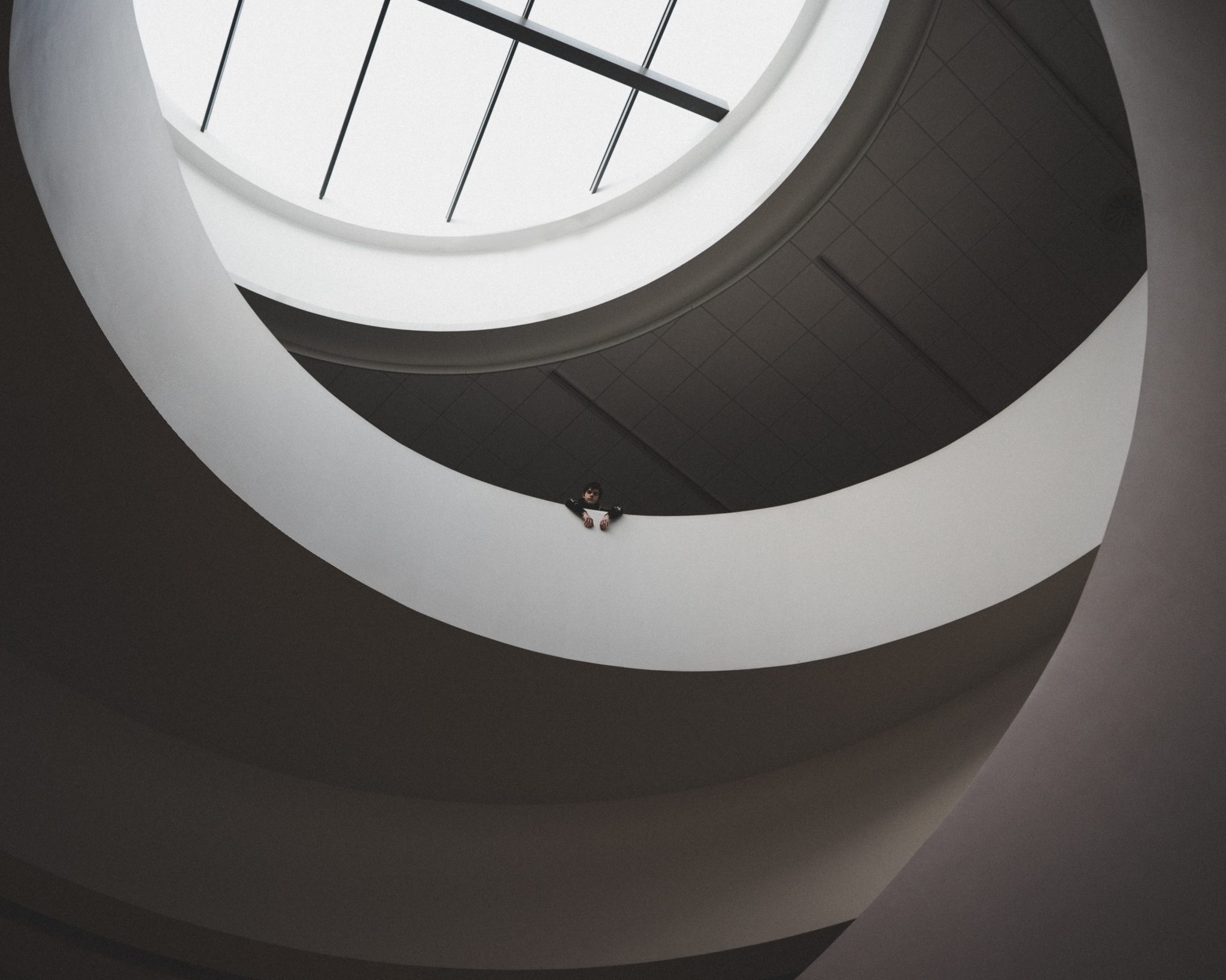 A person leans over a curved white balcony inside a modern building, looking down - buying property in liverpool