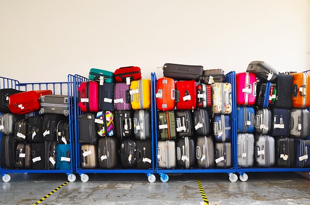 Three blue carts filled with stacked suitcases of various colors and sizes are lined up against a white wall - airbnb luggage storage